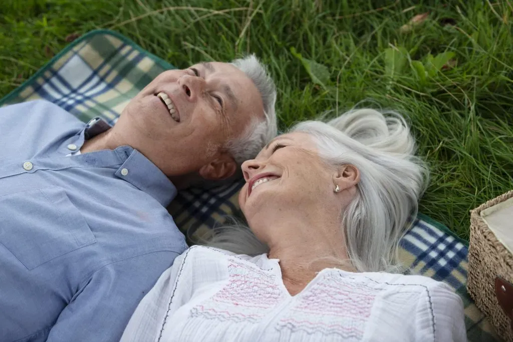 Couple de seniors souriants allongés sur l'herbe pendant un pique-nique.